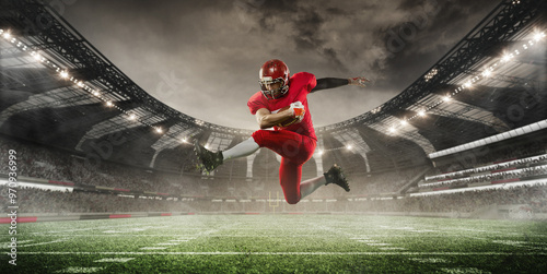 Photos Football player in red uniform is caught mid-air as he leaps high, holding ball tightly, with stadium in background