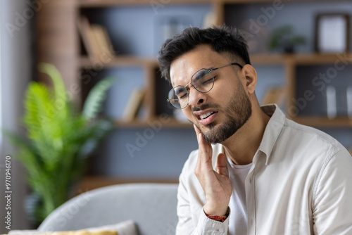 Photography Close-up photo of a young Indian man at home, holding his cheek and suffering fr