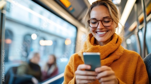 A smiling woman in glasses, dressed warmly in a turtleneck, enjoys a moment on the train while engaging with her phone in a cozy lit environment. photo