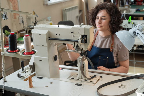 A woman tanner sews a leather belt on a sewing machine. 