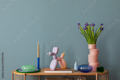 A harmonious display of colorful flowers, pastel candle holders, and quirky modern decor on a wooden shelf, set against a teal wall. Copy space.