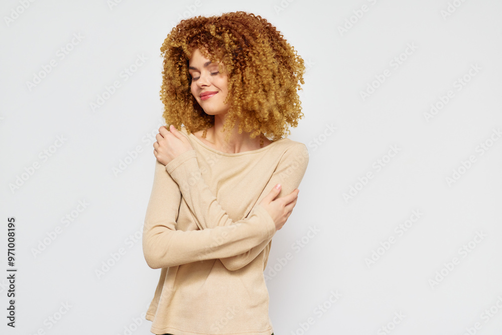 Smiling young woman embracing herself on a plain white background, showcasing self love and positivity, with curly blonde hair and a beige top, radiating warmth and confidence Smiling young woman embracing herself on a plain white background, showcasing self love and positivity, with curly blonde hair and a beige top, radiating warmth and confidence