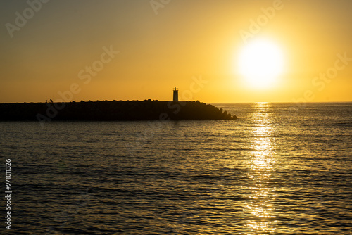 Wallpaper Mural A breathtaking sunset at Nazaré, Portugal, with the sun dipping below the horizon, framed perfectly between two lighthouses at the entrance of the marina, casting golden reflections on the sea. Torontodigital.ca