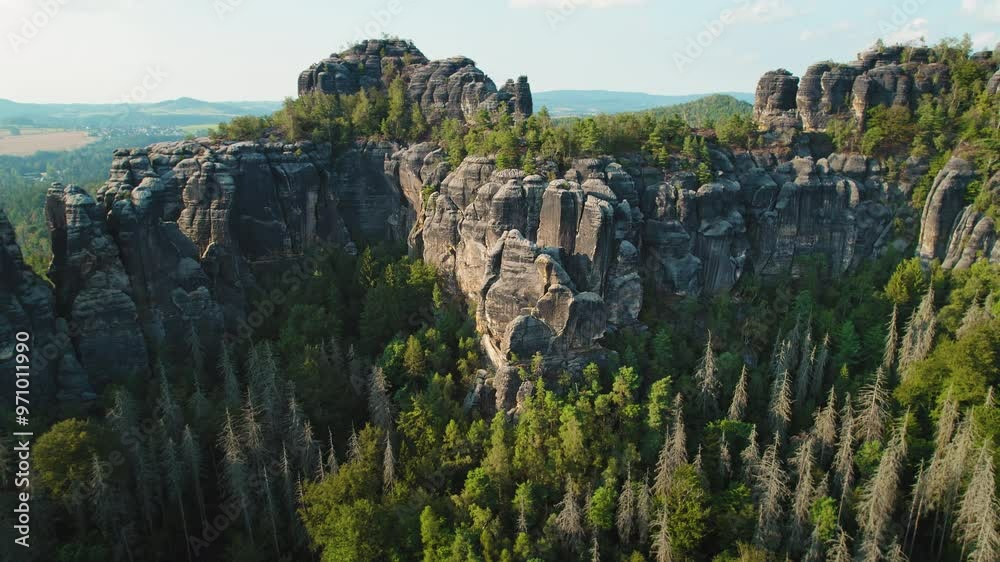 Towering cliffs with jagged edges rise from a dense forest, contrasting the serene surrounding valley. Schrammsteine Geographical feature in Germany. Towering cliffs with jagged edges rise from a dense forest, contrasting the serene surrounding valley. Schrammsteine Geographical feature in Germany.