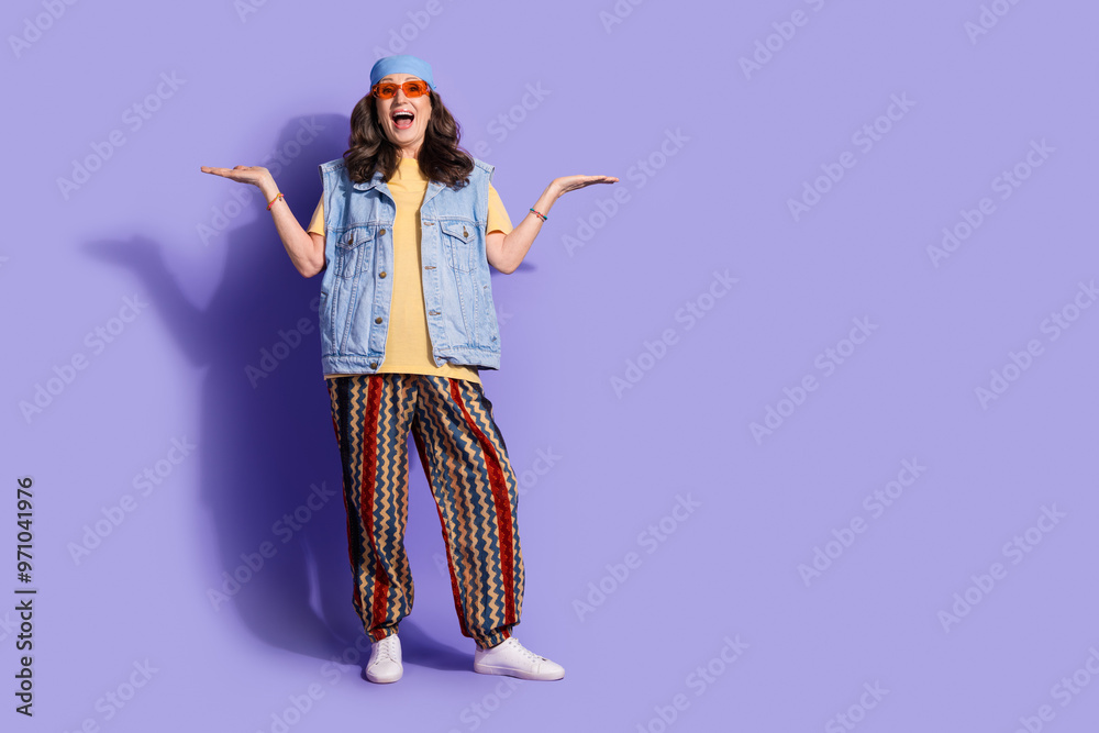 Full size photo of pretty retired woman compare empty space wear trendy denim hipster outfit isolated on violet color background Full size photo of pretty retired woman compare empty space wear trendy denim hipster outfit isolated on violet color background