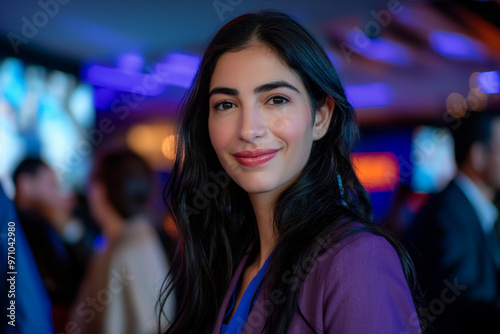 Portrait of an Israeli woman with long black hair, wearing a purple blazer and dark t-shirt smiling