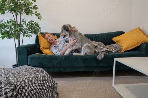 young woman in pajamas with her dog and with a blanket lying on the couch