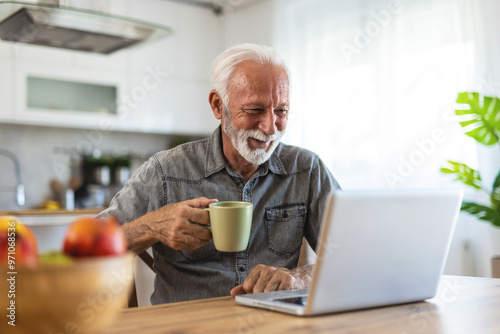 Shot of a senior man sitting alone and using his laptop while enjoying a cup of coffee at home.