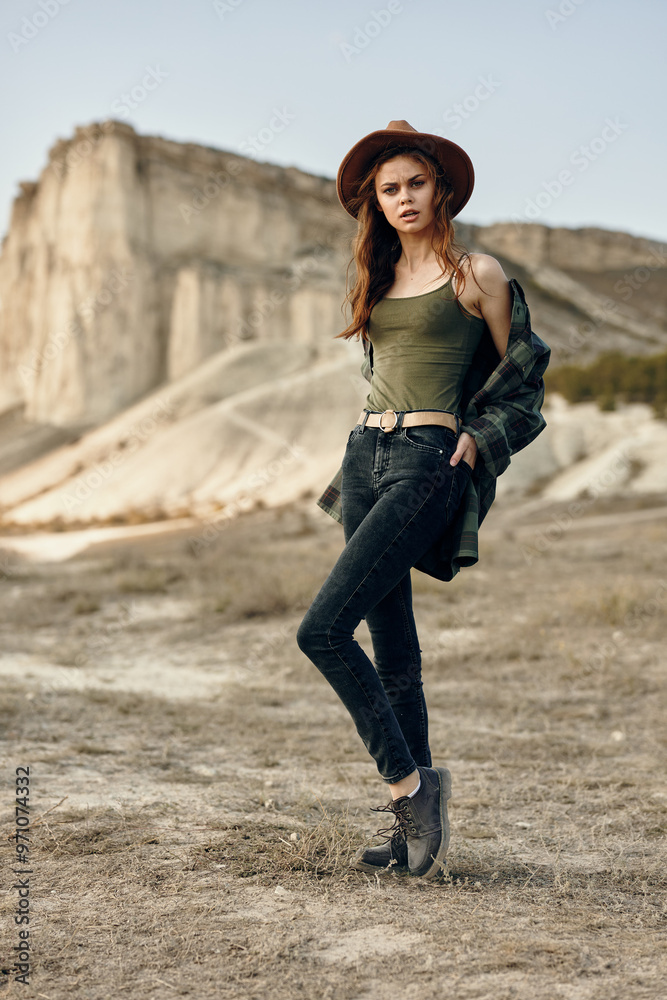 mysterious woman in green shirt and hat standing alone in desert landscape with rock formation