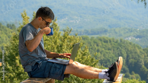 Wallpaper Mural Middle aged man works with laptop and drinks coffee in nature on background of mountains Torontodigital.ca