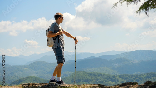 A man on stands on observation deck  with walking sticks and contemplating the mountains. photo