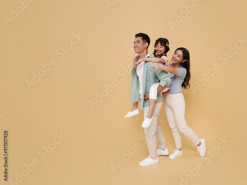 Full body portrait happy asian family standing giving piggyback ride to daughter sit on back isolated on nude color background.