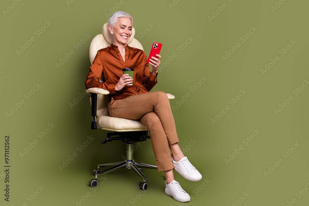 Full size photo of retired female sit office armchair drink coffee device wear brown formalwear isolated on khaki color background