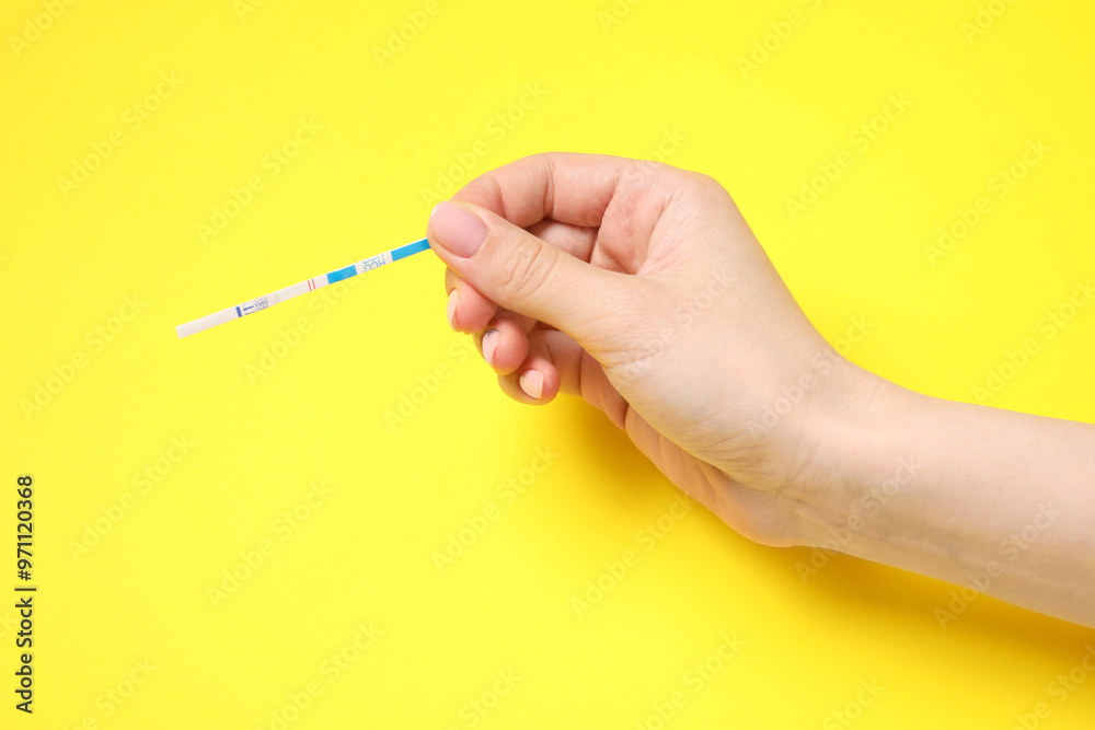 Woman holding pregnancy test on yellow background, closeup Woman holding pregnancy test on yellow background, closeup