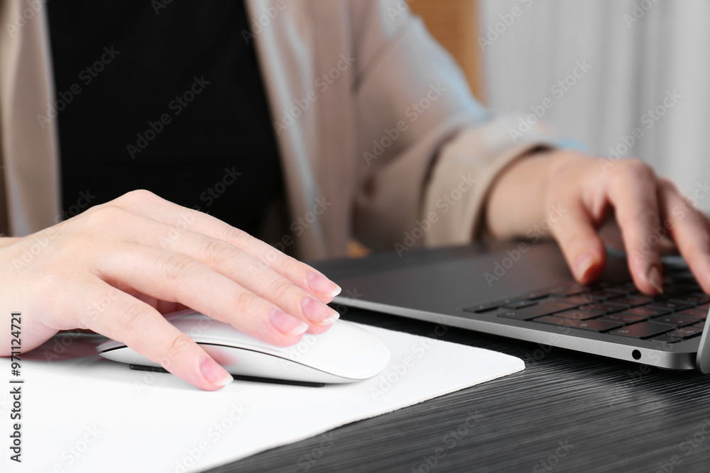 Woman using computer mouse while working with laptop at black wooden table, closeup