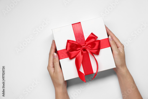 Fototapeta Naklejka Na Ścianę i Meble -  Woman holding gift box with bow on white background, top view