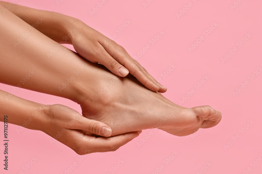 Woman touching her smooth feet on pink background, closeup Woman touching her smooth feet on pink background, closeup