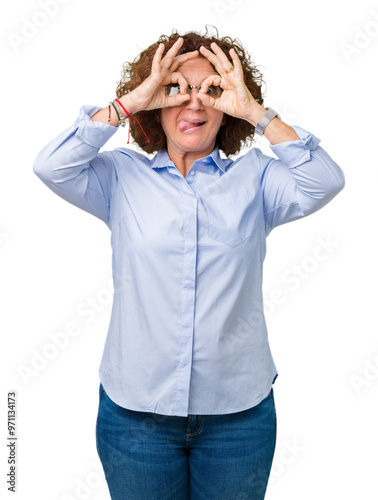 Beautiful middle ager senior businees woman wearing glasses over isolated background doing ok gesture like binoculars sticking tongue out, eyes looking through fingers. Crazy expression.