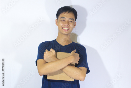 A teenage boy in a navy blue t-shirt is holding a box in the middle of his body and smiling sweetly