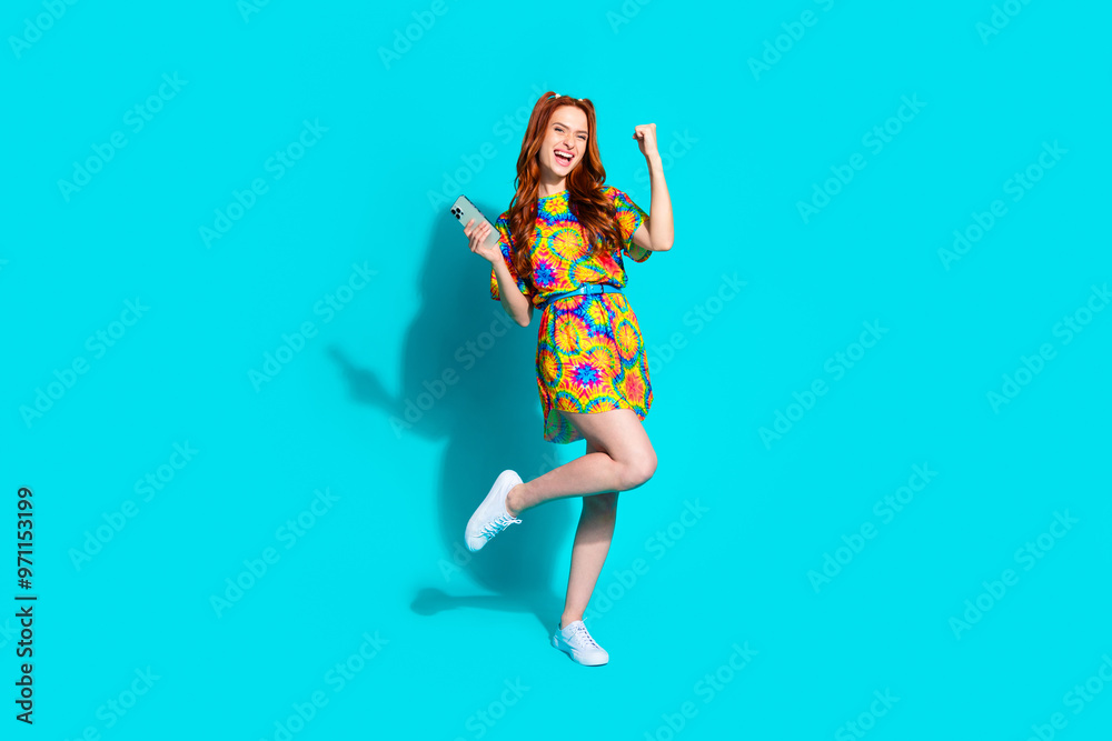 Full length photo of lovely young lady hold device winning dressed stylish colorful garment isolated on cyan color background Full length photo of lovely young lady hold device winning dressed stylish colorful garment isolated on cyan color background