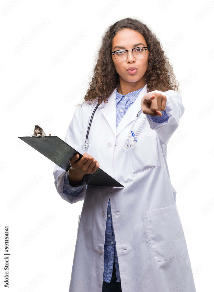 Young hispanic doctor woman holding a clipboard pointing with finger to the camera and to you, hand sign, positive and confident gesture from the front Young hispanic doctor woman holding a clipboard pointing with finger to the camera and to you, hand sign, positive and confident gesture from the front