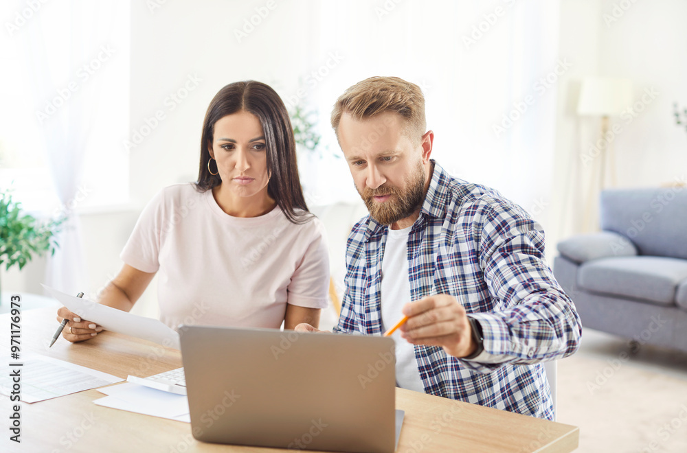 Young married couple sitting at the table with laptop and calculating finances or taxes at home. Man and woman checking utility bills, counting income and profit planning family budget. Young married couple sitting at the table with laptop and calculating finances or taxes at home. Man and woman checking utility bills, counting income and profit planning family budget.