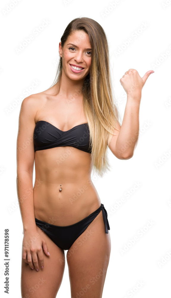 Beautiful young woman wearing black bikini pointing with hand and finger up with happy face smiling Beautiful young woman wearing black bikini pointing with hand and finger up with happy face smiling