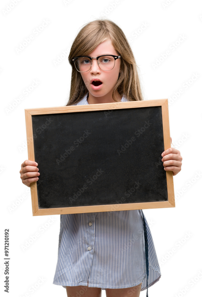 Young blonde child holding blackboard scared in shock with a surprise face, afraid and excited with fear expression Young blonde child holding blackboard scared in shock with a surprise face, afraid and excited with fear expression