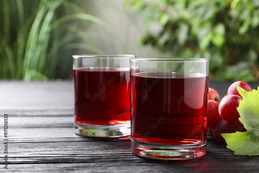 Tasty grape juice in glasses and berries on black wooden table against blurred green background, closeup Tasty grape juice in glasses and berries on black wooden table against blurred green background, closeup