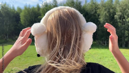 A young girl puts on fluffy warm earmuffs with nature in the background photo