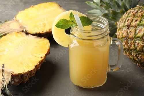 Tasty pineapple juice in mason jar, mint and fruits on grey textured table, closeup photo