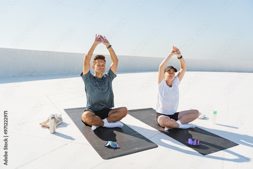 Fototapeta premium A serene image of a man and woman meditating in a yoga pose outdoors on mats, under a clear sky.