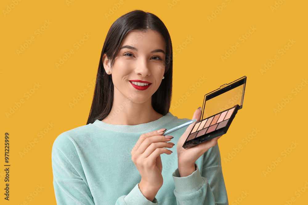 Beautiful young woman with brush and palette of eyeshadows on yellow background Beautiful young woman with brush and palette of eyeshadows on yellow background