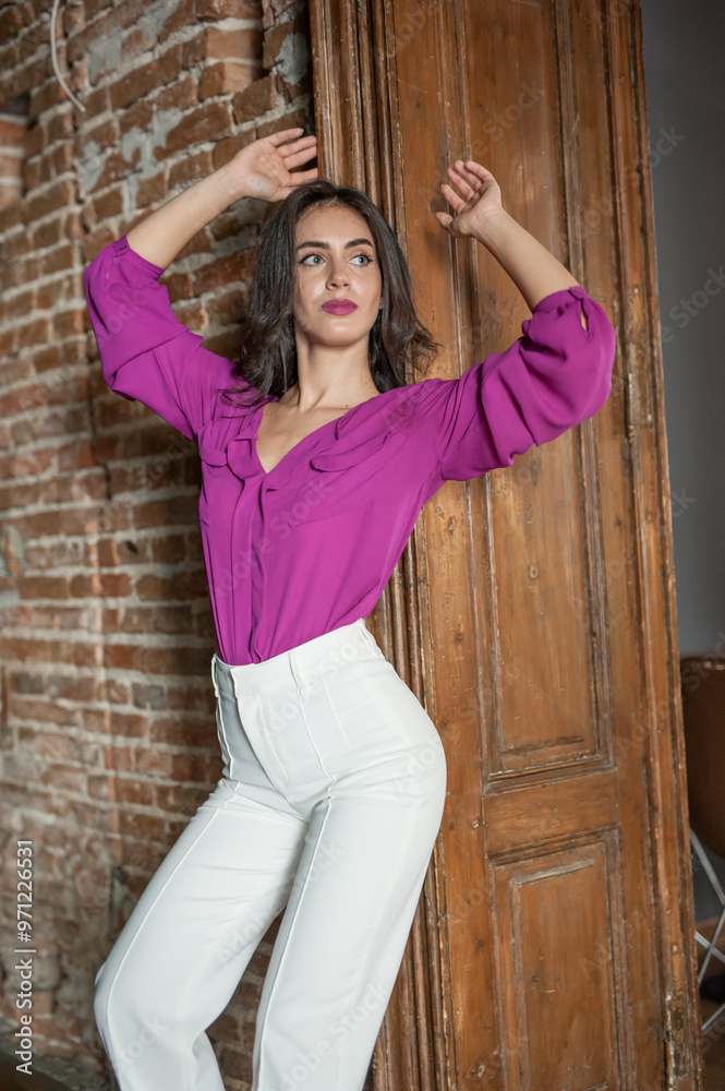 Beautiful young brunette woman in a purple blouse and white pants posing outdoor. Portrait of a beautiful young brunette woman with long hair posing fashion