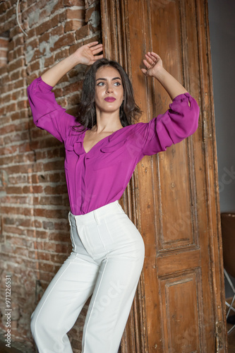 Obraz na płótnie Beautiful young brunette woman in a purple blouse and white pants posing outdoor. Portrait of a beautiful young brunette woman with long hair posing fashion w salonie