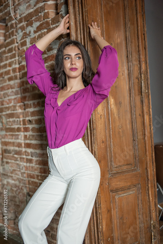 Obraz na płótnie Beautiful young brunette woman in a purple blouse and white pants posing outdoor. Portrait of a beautiful young brunette woman with long hair posing fashion w salonie