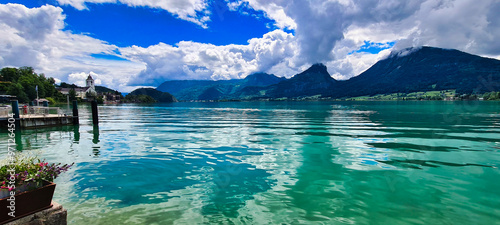 A serene view of Wolfgangsee, one of Austria's most beautiful lakes, with crystal-clear waters surrounded by majestic mountains. The vibrant colors and peaceful setting make this a perfect spot for re