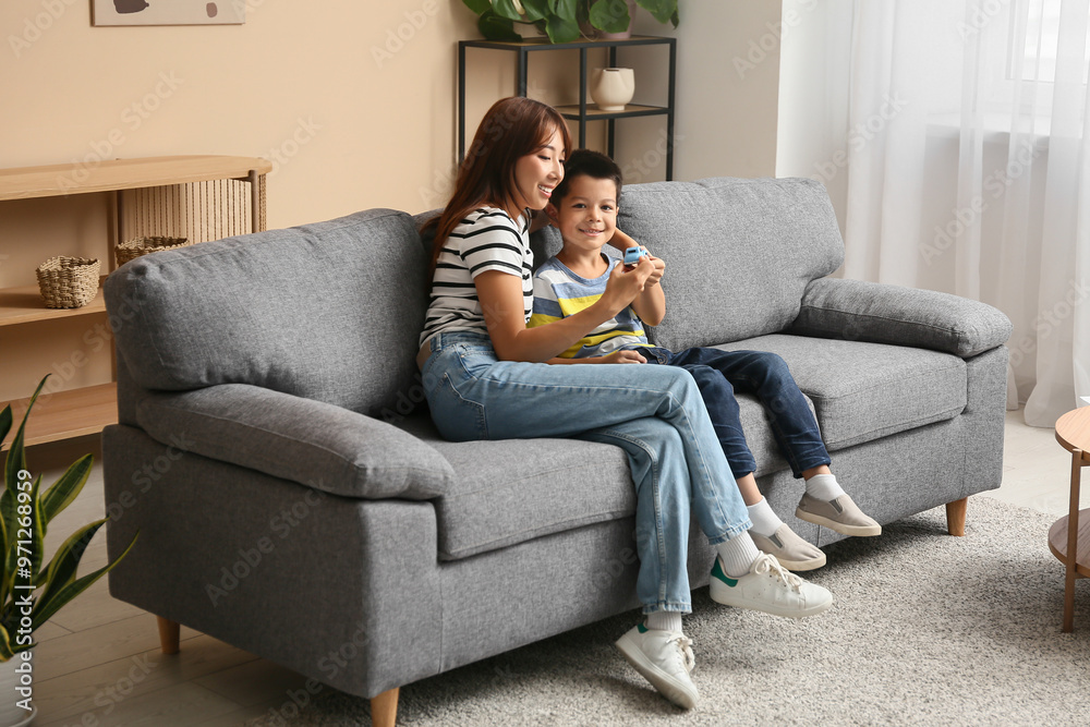 Beautiful young happy Asian mother and cute little son plying with toy on sofa at home Beautiful young happy Asian mother and cute little son plying with toy on sofa at home