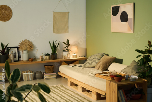 Medium-sized comfortable couch with three cushions and bamboo tray with teapot standing in the corner of spacious living room