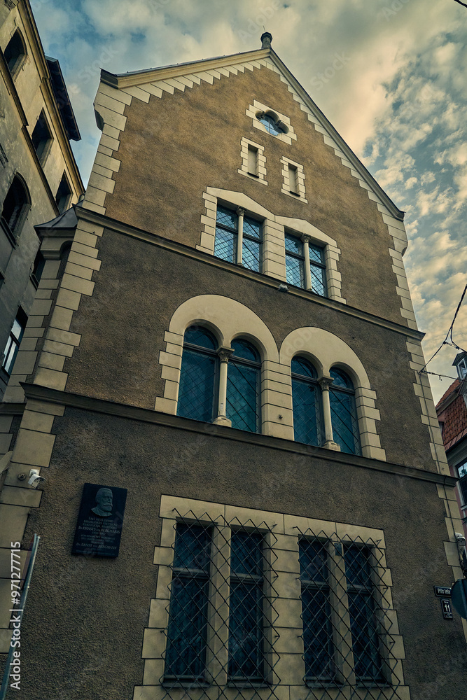 Obraz premium A close-up of a historic building in Riga, Latvia, showcasing its intricate brickwork and architectural details. The building's facade features a prominent arched window and a decorative plaque.