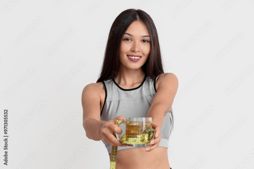 Beautiful young happy Asian woman with measuring tape and cup of tea for weight loss on white background Beautiful young happy Asian woman with measuring tape and cup of tea for weight loss on white background