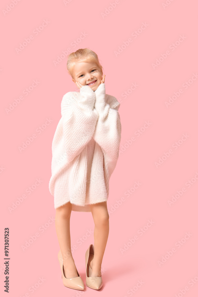Cute little happy girl in warm stylish sweater and in oversized high heels on pink background Cute little happy girl in warm stylish sweater and in oversized high heels on pink background