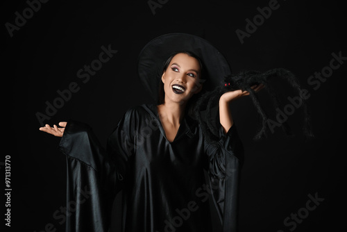 Beautiful young happy witch with spider on black background photo