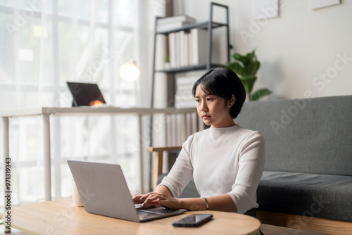 Focused asian freelancer working on laptop at home office