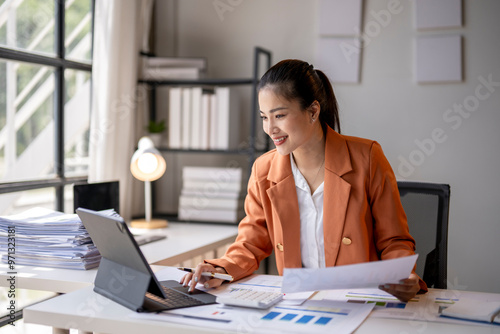 Asian accountant woman working with documents using calculator and laptop computer at office desk
