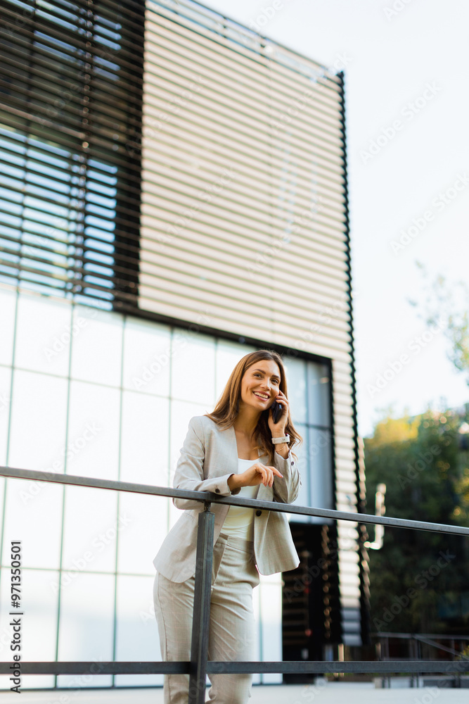 Fototapeta premium Smiling business woman enjoying a sunny day outdoors while texting on her smartphone near modern architecture in an urban setting
