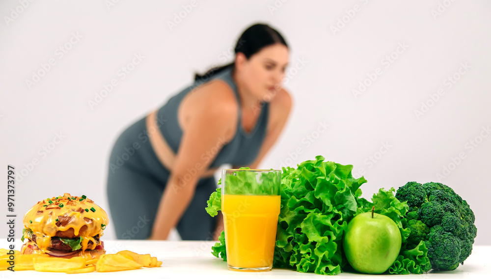Beautiful, full-figured woman exercising on a light background with a burger and greens nearby. Perfect for promoting a healthy lifestyle and the balance between fitness and nutrition. Beautiful, full-figured woman exercising on a light background with a burger and greens nearby. Perfect for promoting a healthy lifestyle and the balance between fitness and nutrition.