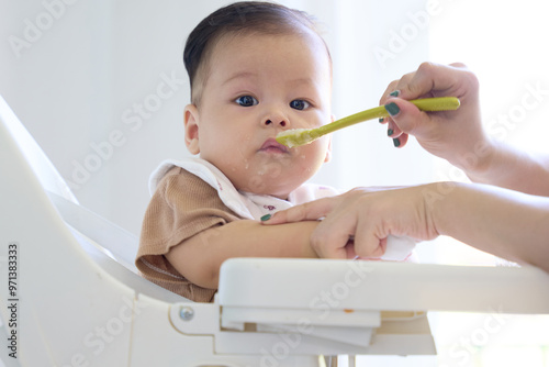 The mother holds the baby's hand, and feeds the baby, the baby looks at the camera, the natural space and the white light. photo