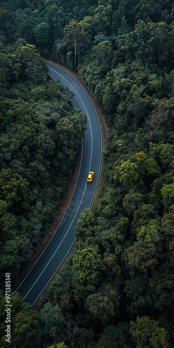 Top down view of curvy, asphalt road surrounded by bunch of evergreen trees. car driving on the road. Beautiful aerial view of dense forest mountain landscape in summer time with curvy road cutting th