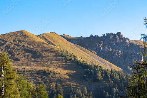 Lush green slopes lead up to rocky mountain peak Latschur in Gailtal Alps, Carinthia, Austria. Serene alpine landscape in warm glow of morning sun in summer. Peaceful serene atmosphere Austrian Alps photo